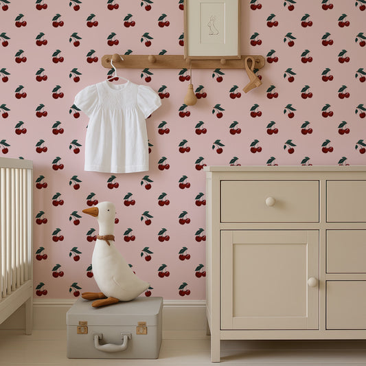 a nursery room with a pink wall decorated with a repeating pattern of cherries. A white dress is hanging on a wooden hanger, and a stuffed duck is sitting on a gray suitcase in the foreground.