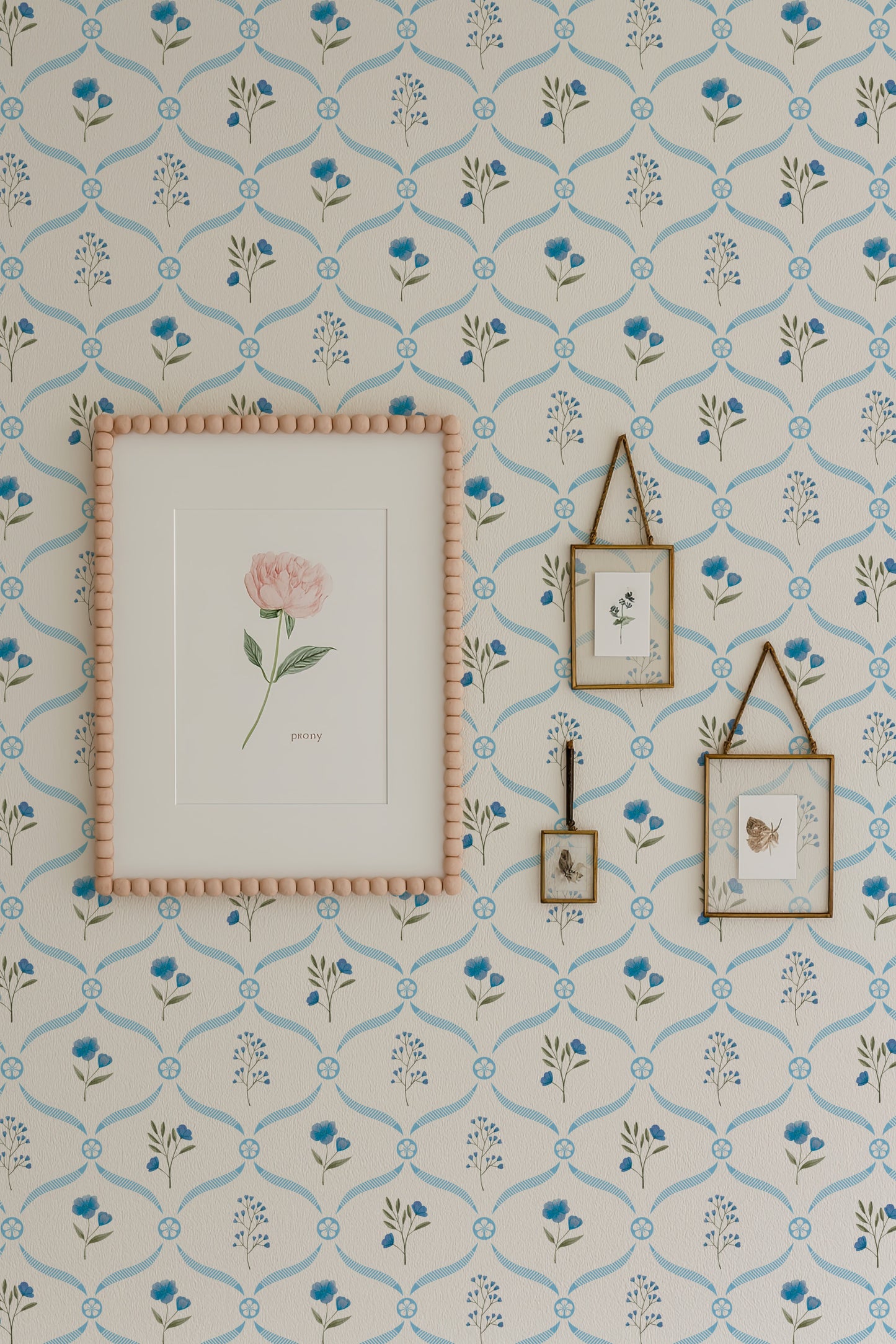 a wall adorned with a floral wallpaper pattern, complemented by a framed picture of a pink rose and two framed pictures hanging on the wall.