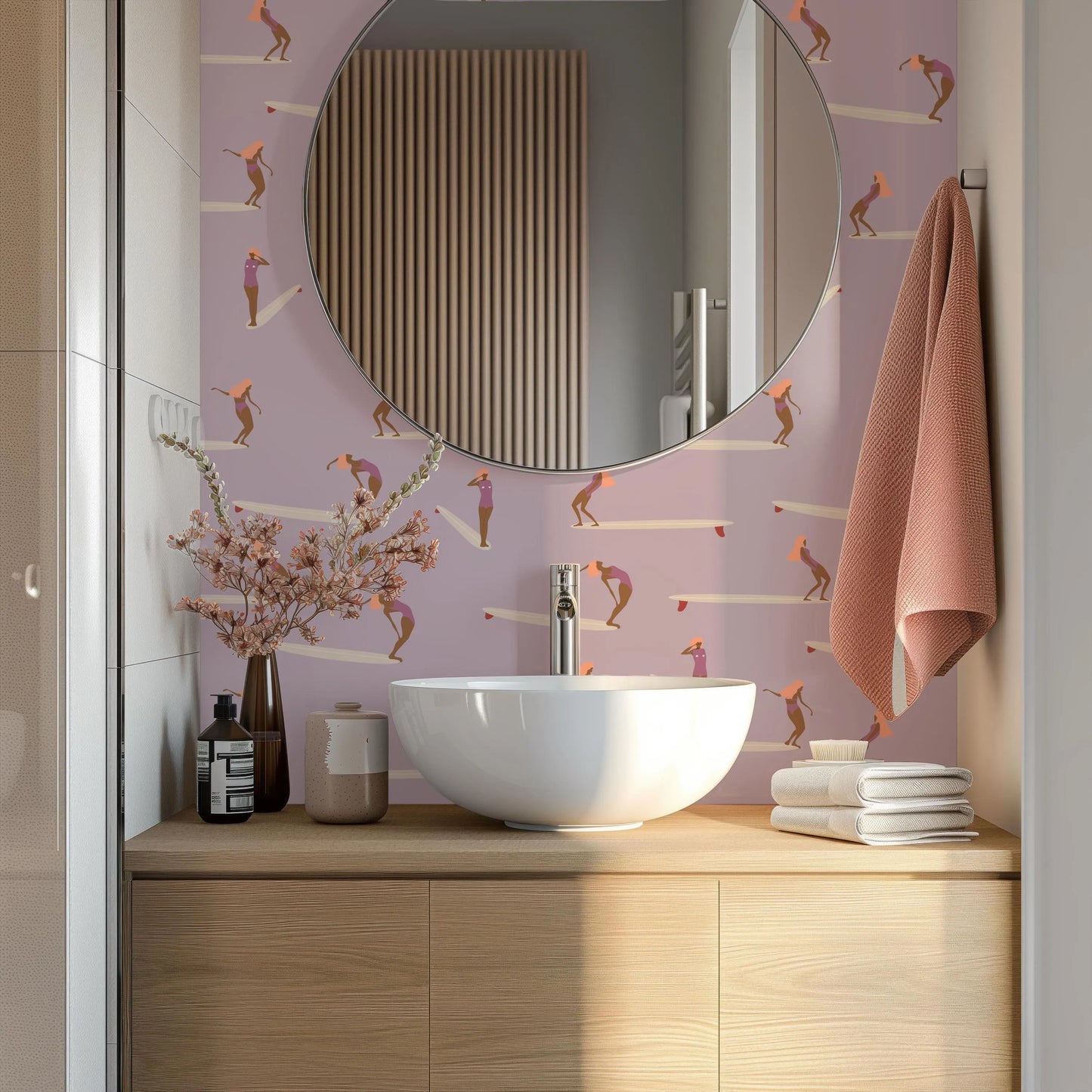 a bathroom with a white sink, a round mirror, and a pink wall with a pattern of people. The bathroom also includes a wooden vanity and various decorative items such as a vase with flowers and a folded towel.