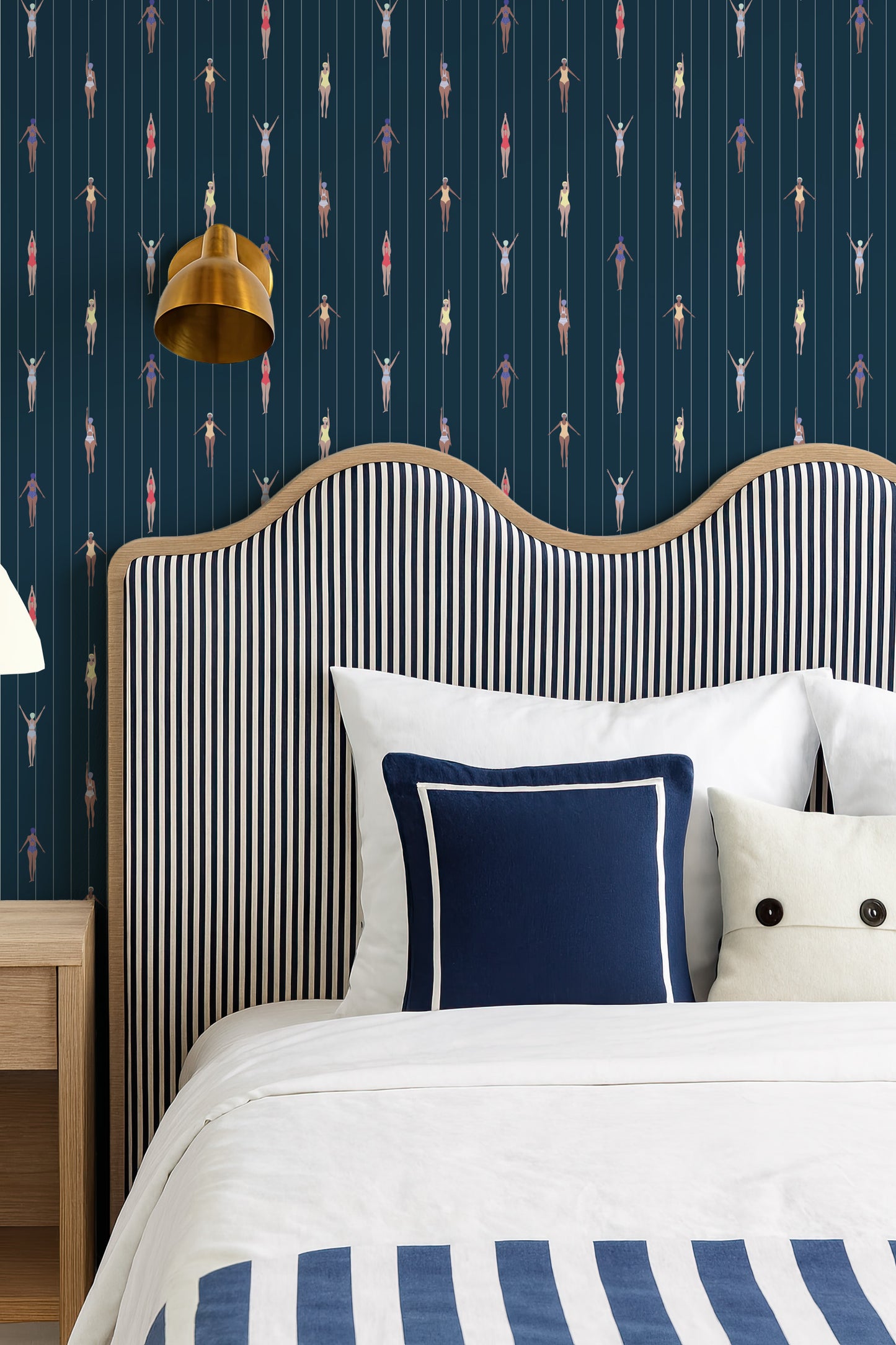 a bedroom with a striped headboard and a white bed with blue and white striped bedding. The wall behind the bed has a pattern of colorful figures, creating a vibrant and lively atmosphere.