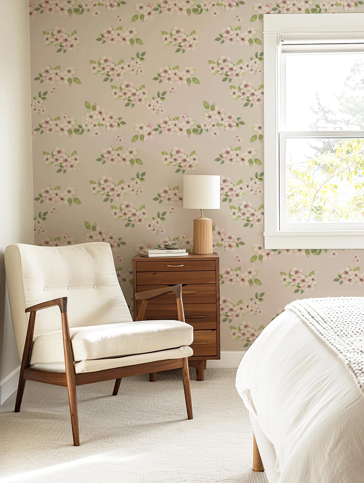 a cozy bedroom with a floral wallpaper, a white armchair, a wooden side table with a lamp, and a window with white blinds.