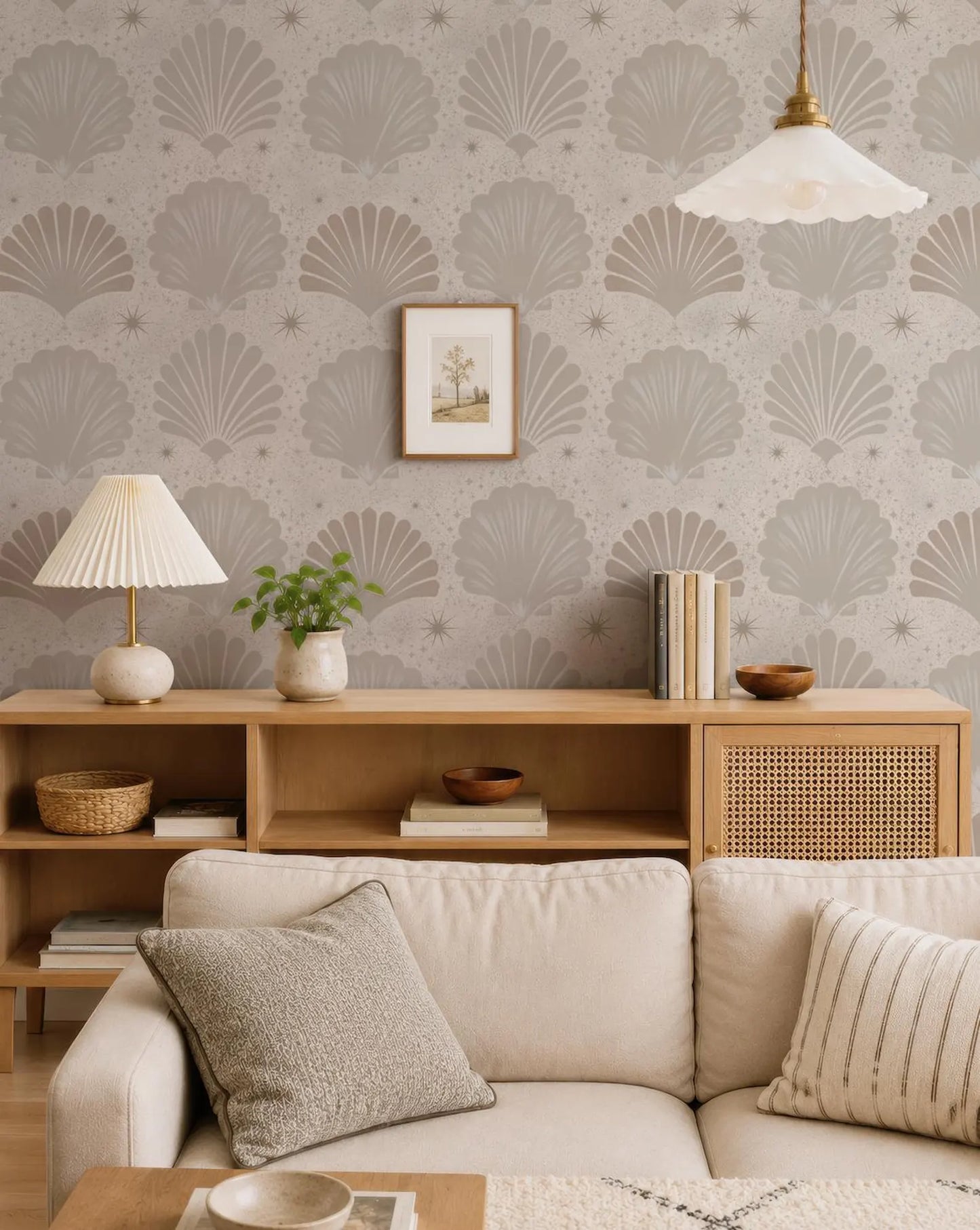a cozy living room with a beige sofa, a wooden side table, and a lamp. The wall behind the furniture is covered in a patterned wallpaper with a repeating design of seashells and stars. The room also features a potted plant, a framed picture, and a bookshelf with various books and decorative items.