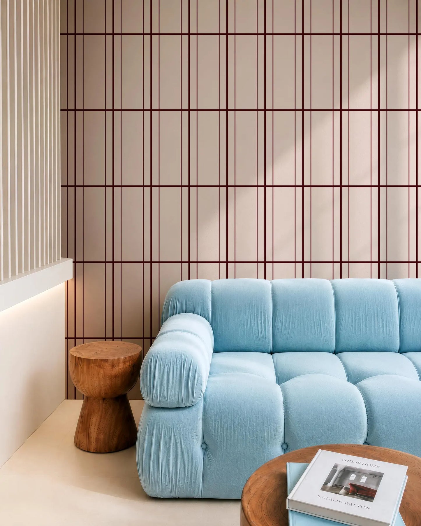 a modern living room with a blue sofa, a wooden side table, and a wooden coffee table. The walls are adorned with a geometric pattern in shades of pink and white, and the room has a minimalist and clean design.