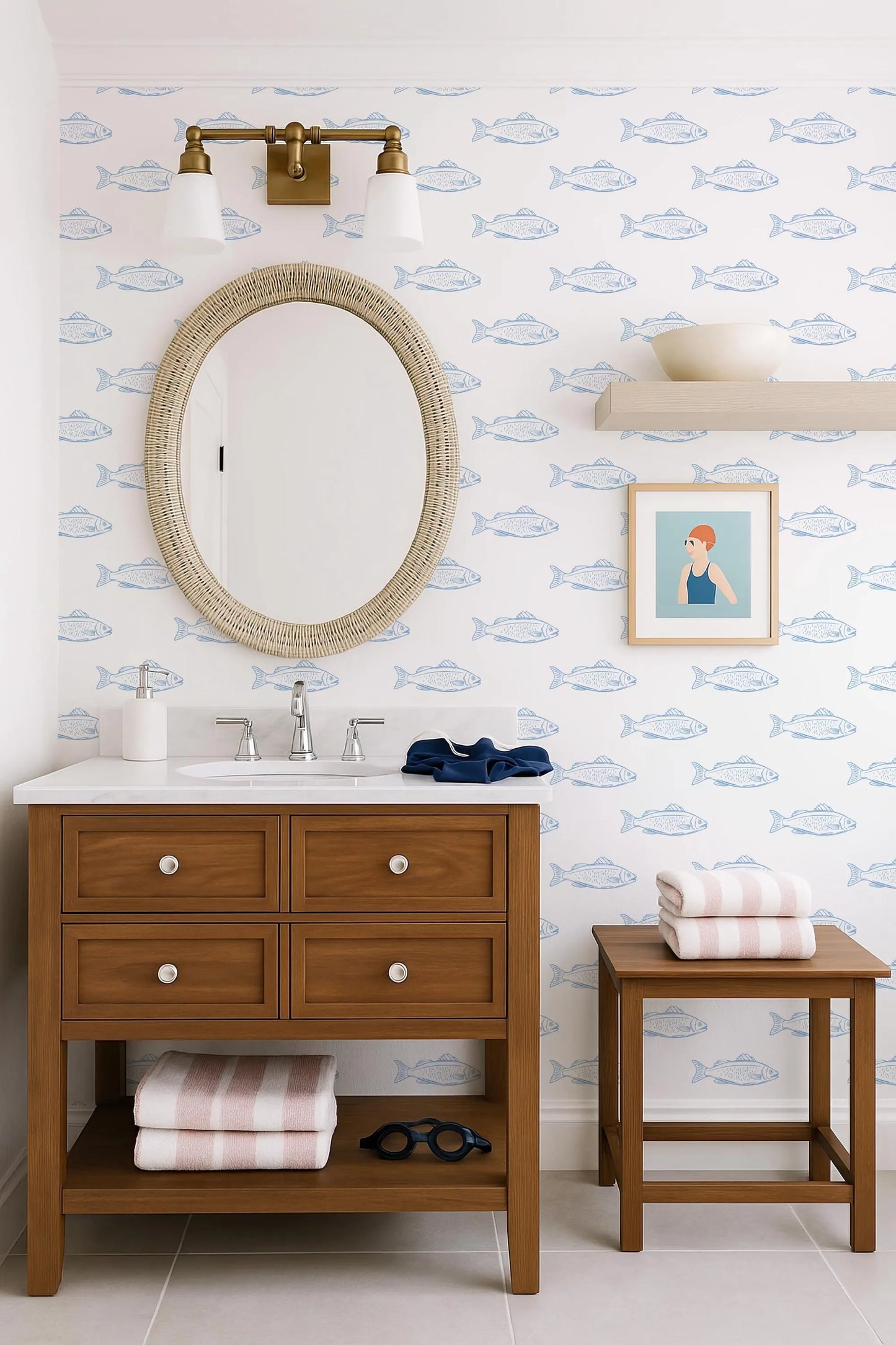 a bathroom with a wooden vanity, a round mirror, and a framed picture of a woman. The walls are decorated with a blue and white fish wallpaper, and there is a shelf with a bowl and a towel.