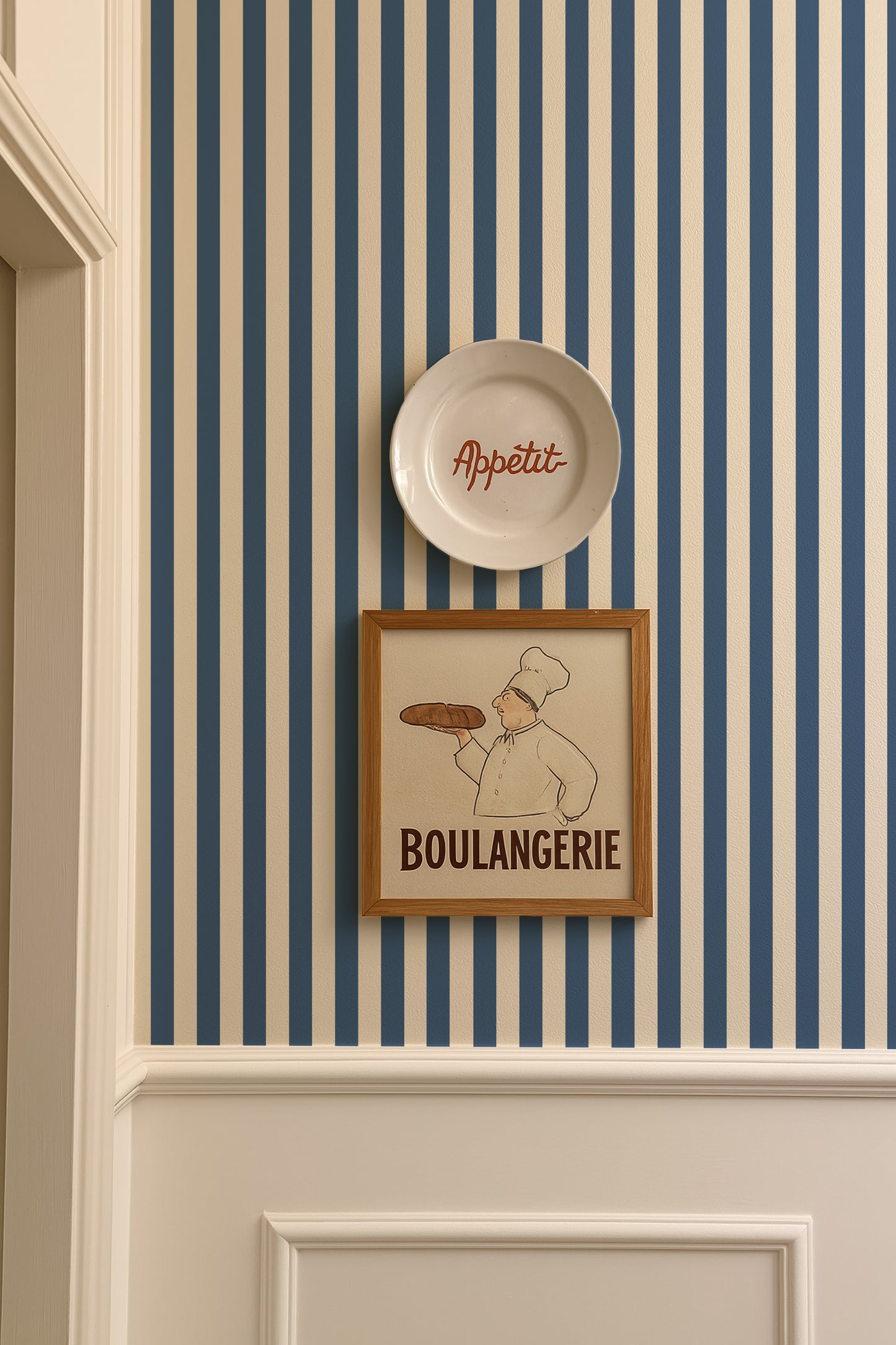 a framed illustration of a chef holding a loaf of bread, with the word "Boulangerie" written below the image. The chef is wearing a chef's hat and apron, suggesting a bakery setting. The image also includes a plate with the word "Appétit" written on it, indicating that the chef is serving a meal.