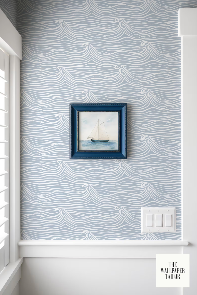 a framed painting of a sailboat on a blue background, hanging on a wall with a wave-patterned wallpaper.