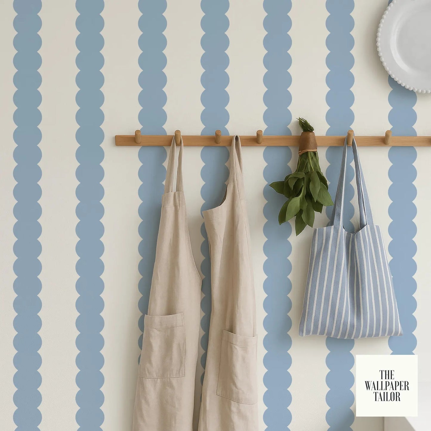 a wall with blue and white striped wallpaper, a wooden hanger with two aprons hanging on it, and a small potted plant placed on the wall.