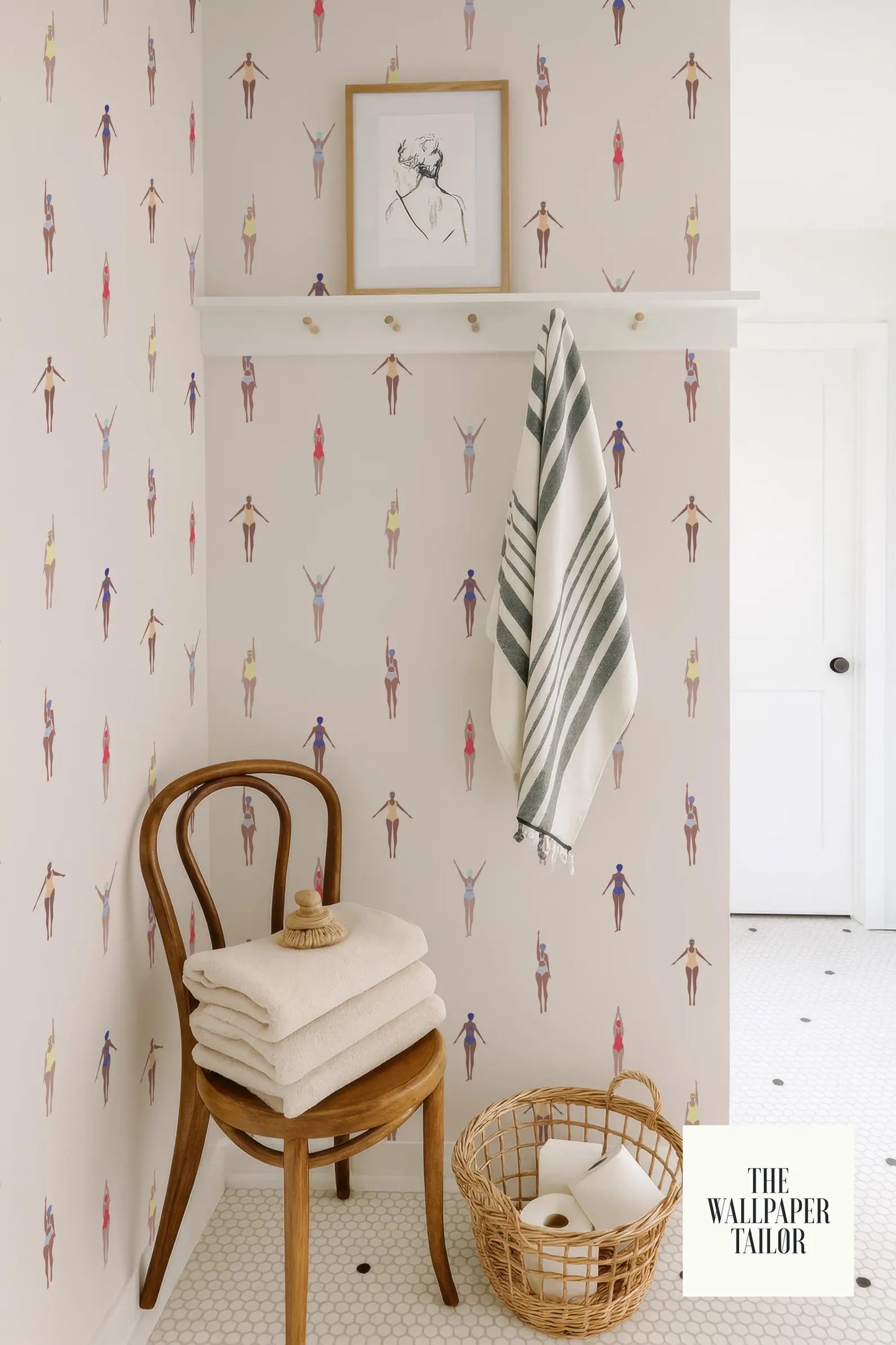 a bathroom with a wooden chair, towels, and a basket of toilet paper. The walls are decorated with a pattern of colorful figures, and there is a framed picture above the chair.