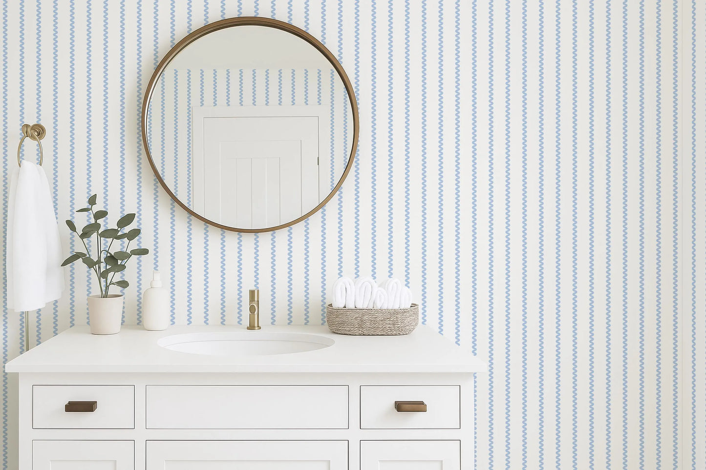 a bathroom with a white sink, a round mirror, and a white cabinet. The bathroom has a striped blue and white wallpaper, and there is a plant on the counter.