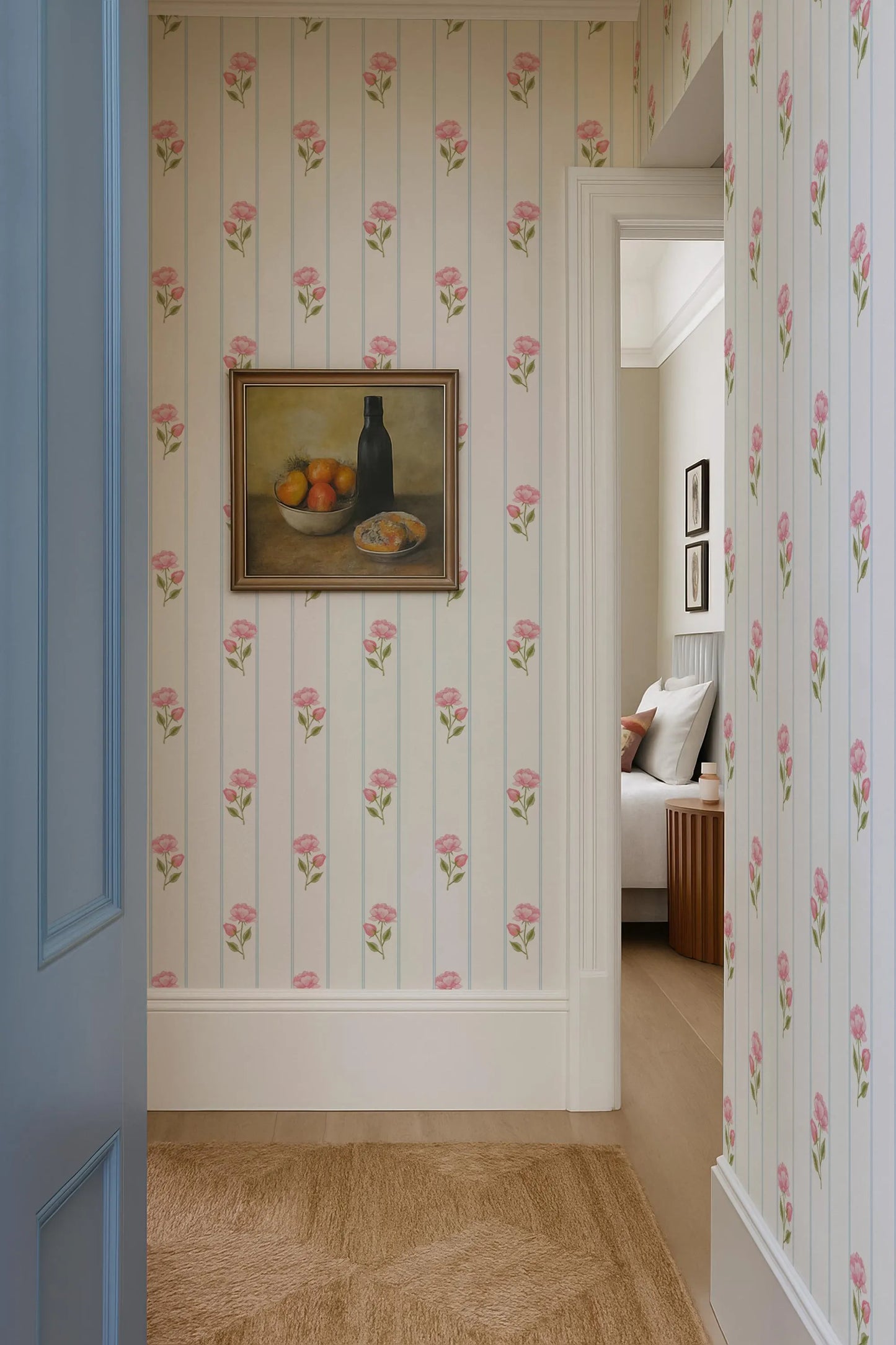 a hallway with a framed painting of a still life of fruit on the wall, a blue door, and a wooden floor.