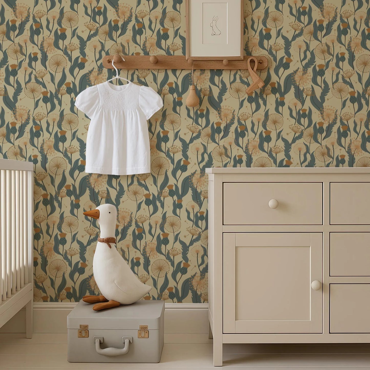 a nursery room with a white dress hanging on a wooden hanger, a stuffed duck sitting on a suitcase, and a wooden shelf with a picture frame above it. The room has a floral wallpaper and a white dresser.