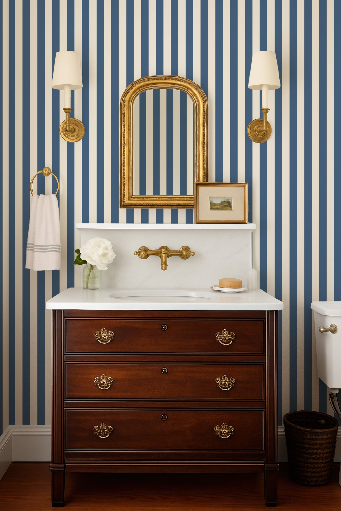 a bathroom with a wooden dresser, a white sink, and a mirror above it. The walls are striped in blue and white, and there are two wall sconces on either side of the mirror.
