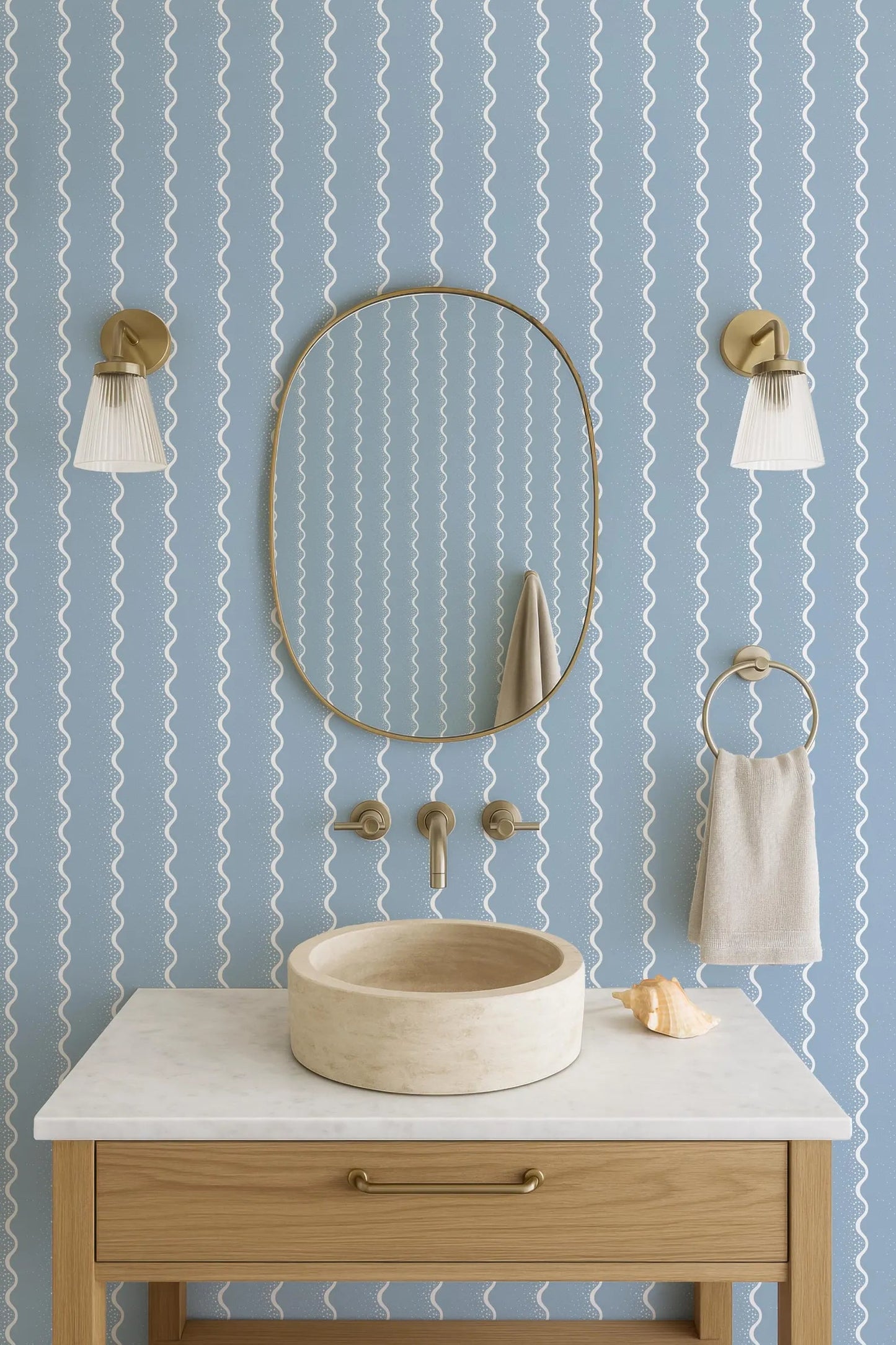 a bathroom with a white marble sink, a round mirror, and two wall sconces. The walls are covered in a blue and white striped pattern, creating a modern and stylish atmosphere.
