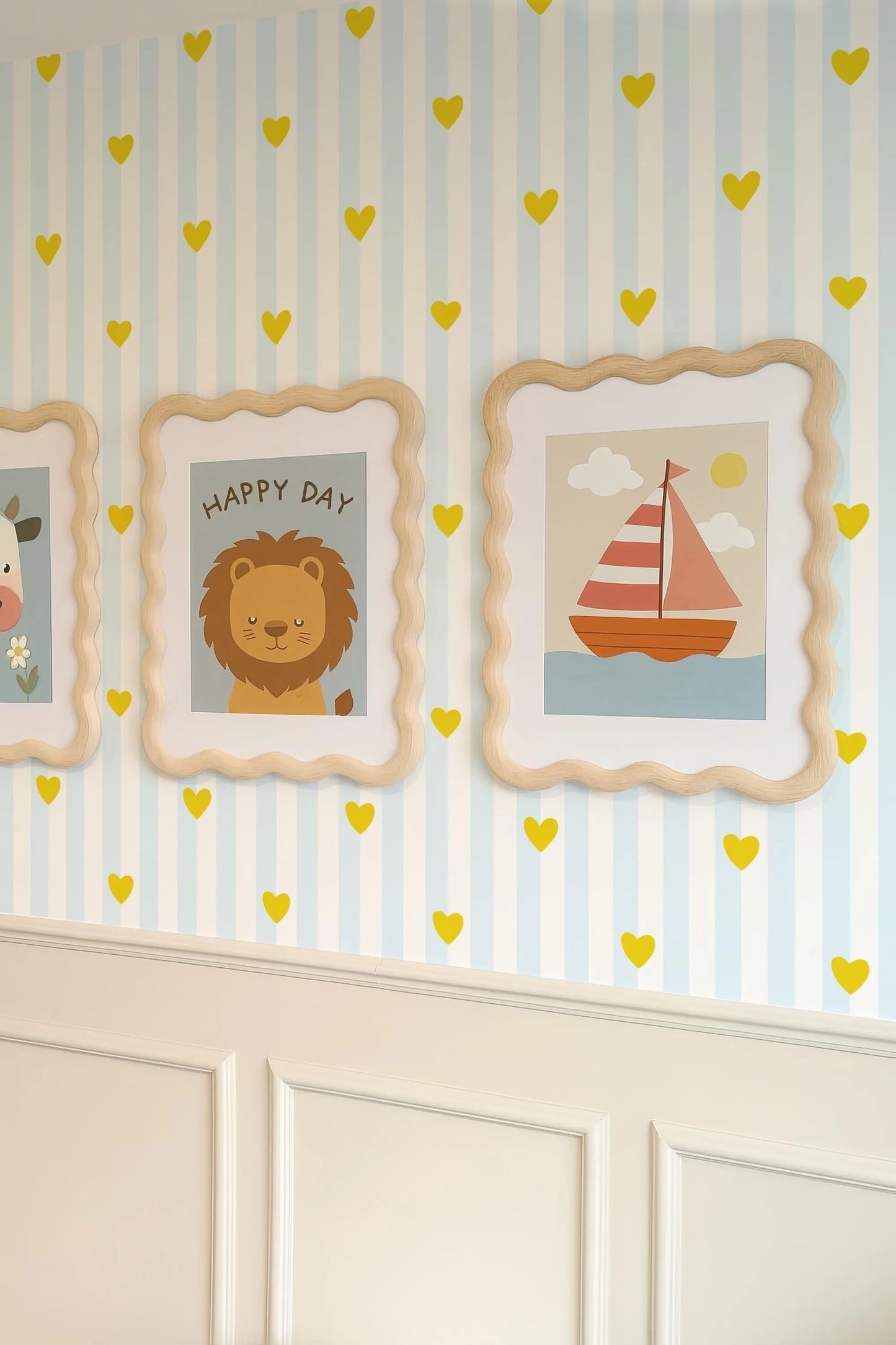 a wall decorated with three framed pictures, each depicting a different scene. The pictures include a lion, a sailboat, and a heart-shaped design. The wall is adorned with yellow heart-shaped stickers scattered throughout, creating a cheerful and playful atmosphere.