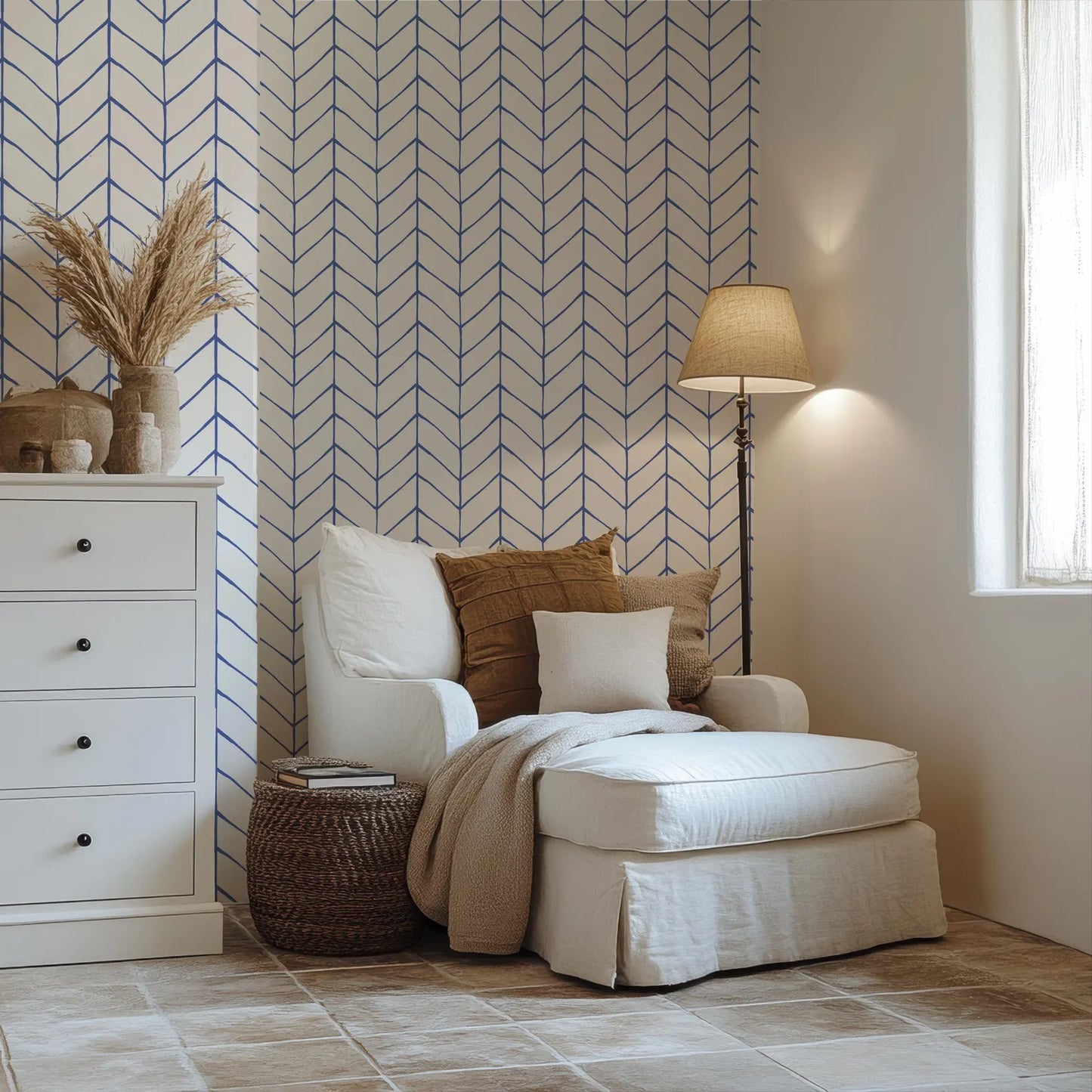a cozy and inviting living room with a white armchair, a white ottoman, and a white side table. The room is decorated with a blue and white chevron pattern on the wall, and there is a lamp on a side table next to the armchair.
