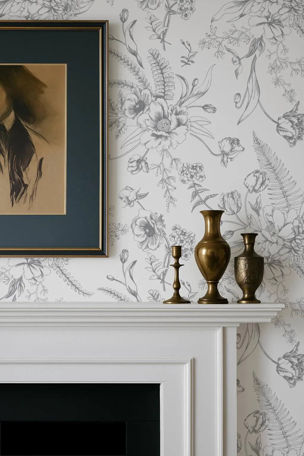 a white fireplace mantel with three decorative items on it, including two brass vases and a framed picture. The mantel is set against a wall with a floral wallpaper pattern.