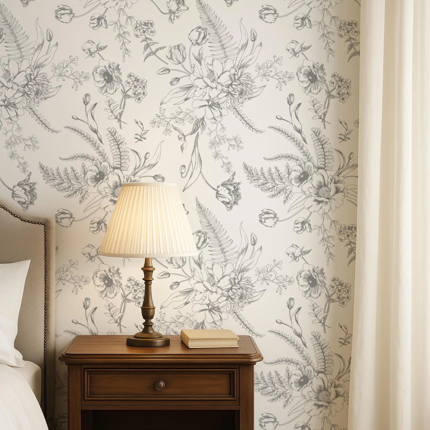 a bedroom setting with a wooden nightstand, a lamp, and a book on the nightstand. The wall behind the nightstand has a floral wallpaper pattern.