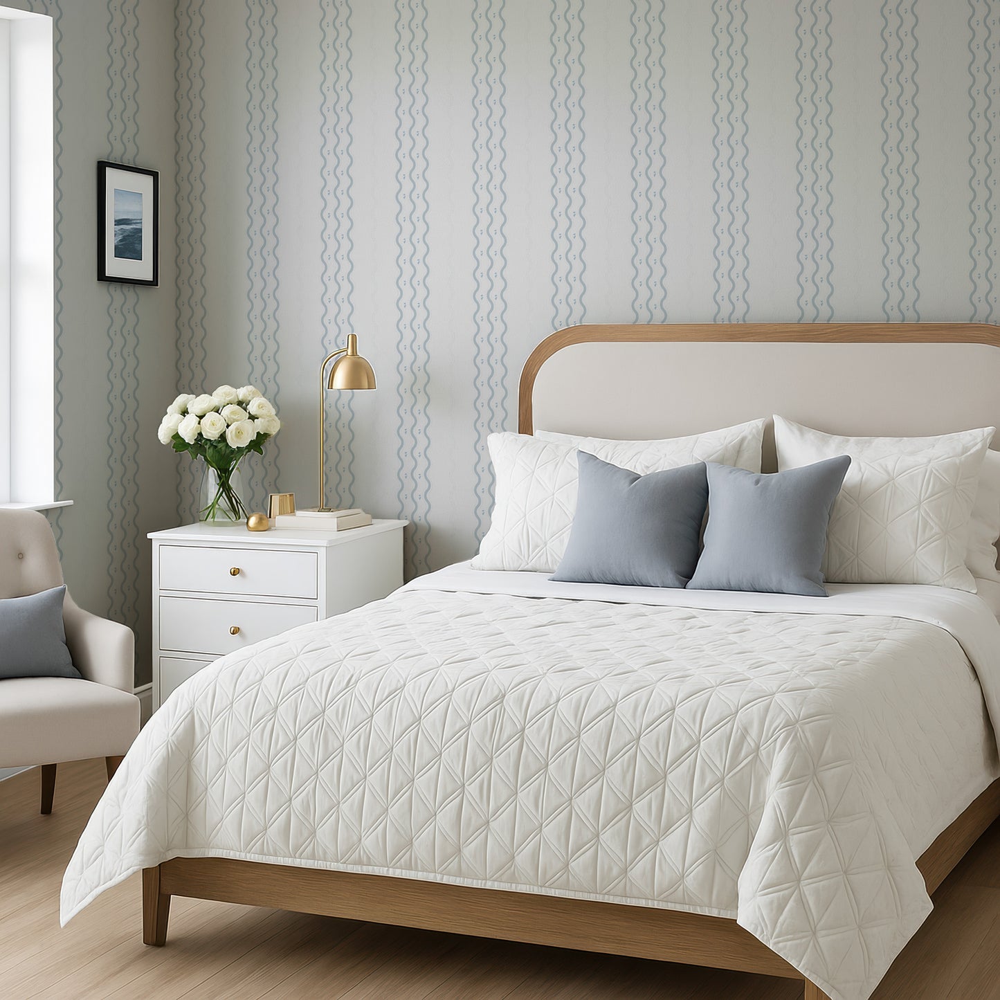 a well-furnished bedroom with a large bed, a nightstand, and a chair. The bed has a white comforter and a wooden headboard, and the room has a neutral color scheme with gray and white walls and a wooden floor.