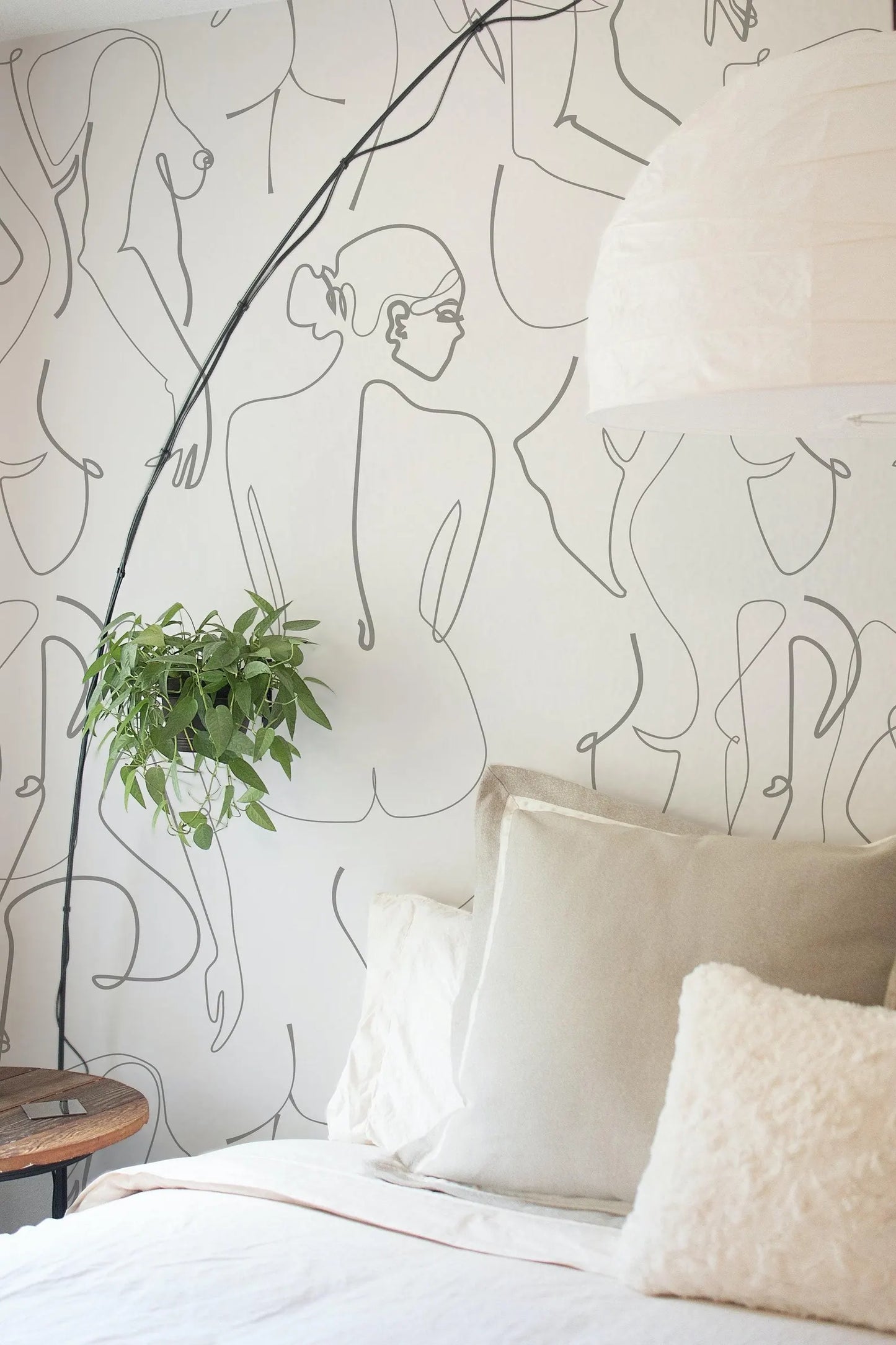 a bedroom with a white bed, a potted plant, and a wall with abstract line drawings of human figures.