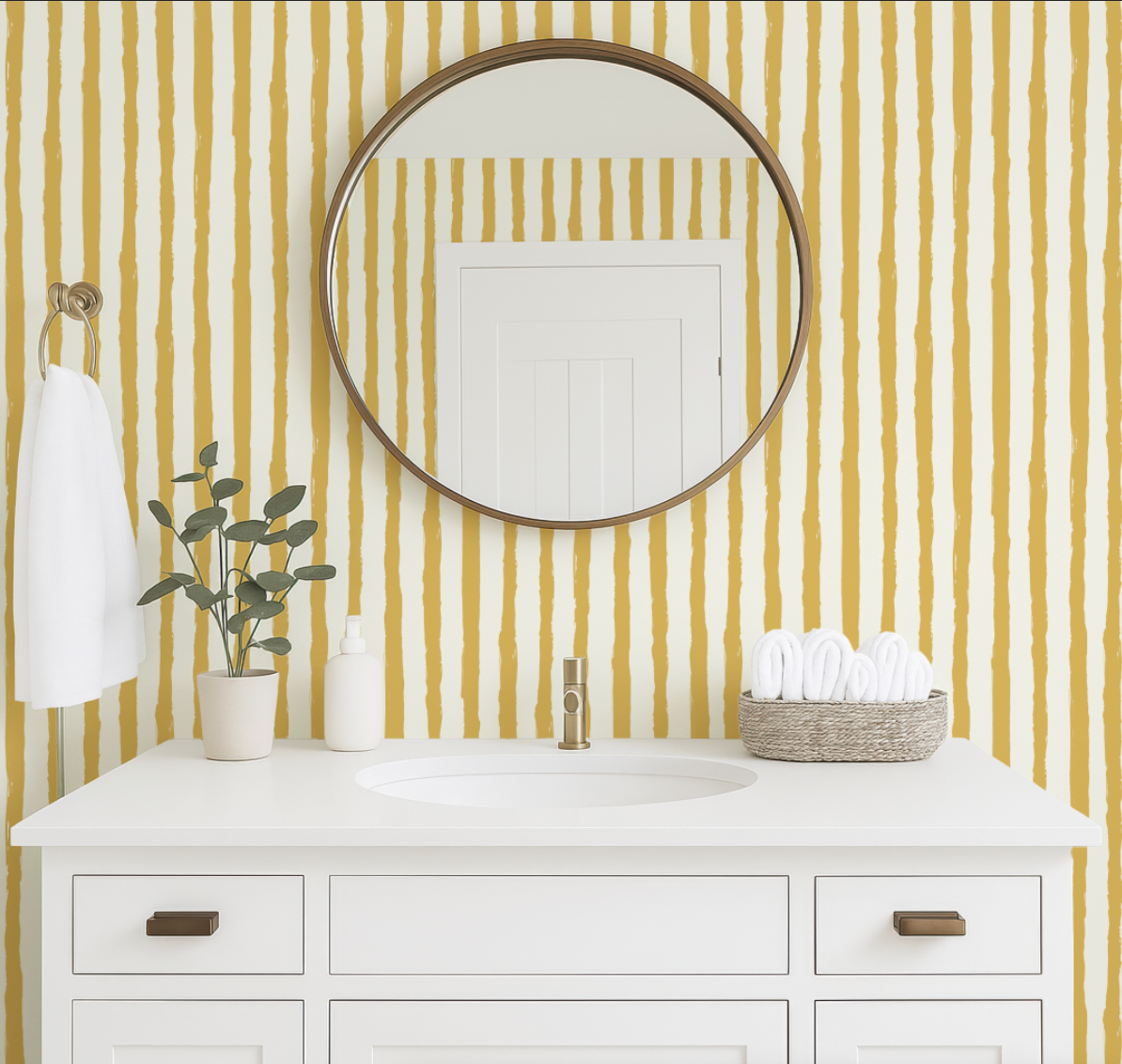 a bathroom vanity with a white countertop, a round mirror above it, and a plant on the counter. The walls are covered in yellow and white striped wallpaper, and there is a basket of folded towels on the counter.