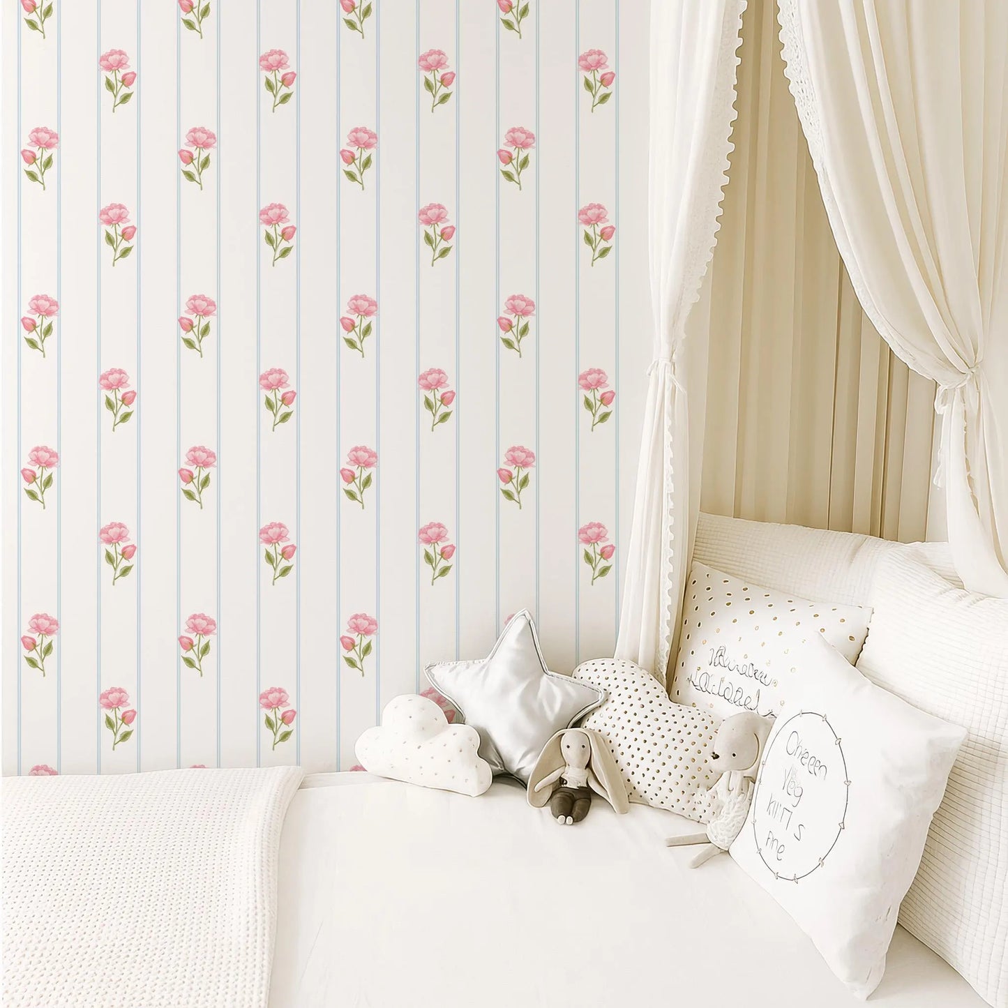 a cozy and inviting bedroom scene, featuring a bed with white linens and a canopy, a wallpapered wall with a repeating pattern of pink flowers, and a collection of stuffed animals and decorative pillows on the bed.