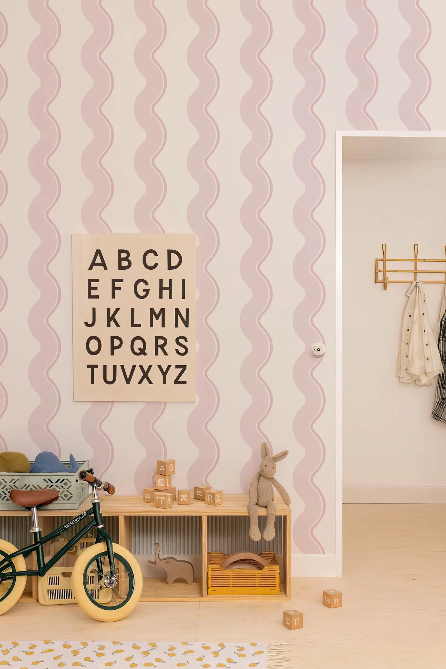 a child's bedroom with a pink and white striped wallpaper, a wooden toy shelf, a bicycle, and a toy rabbit.