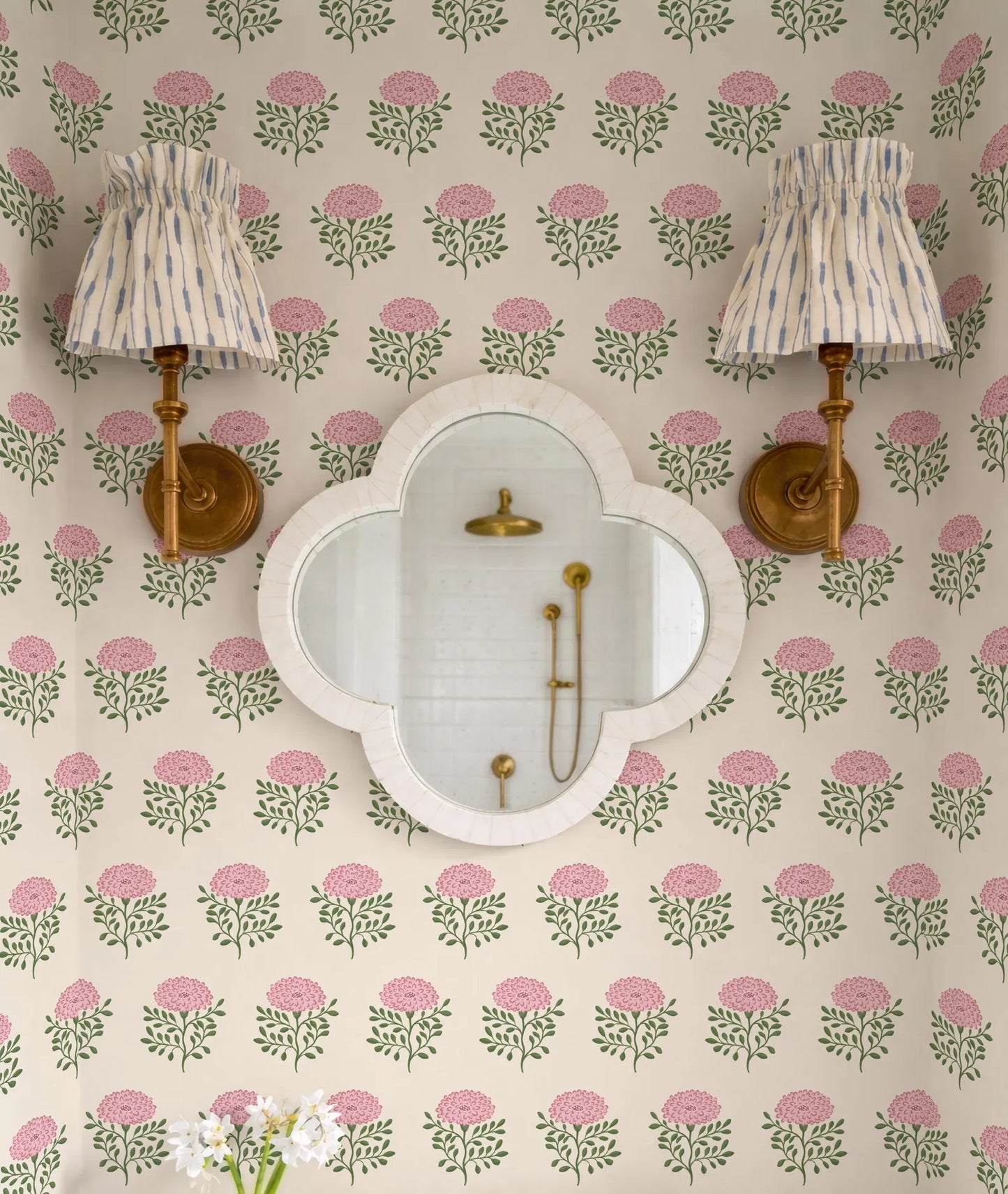 a bathroom with a floral wallpaper pattern, a white oval mirror, and two wall sconces with striped fabric shades.