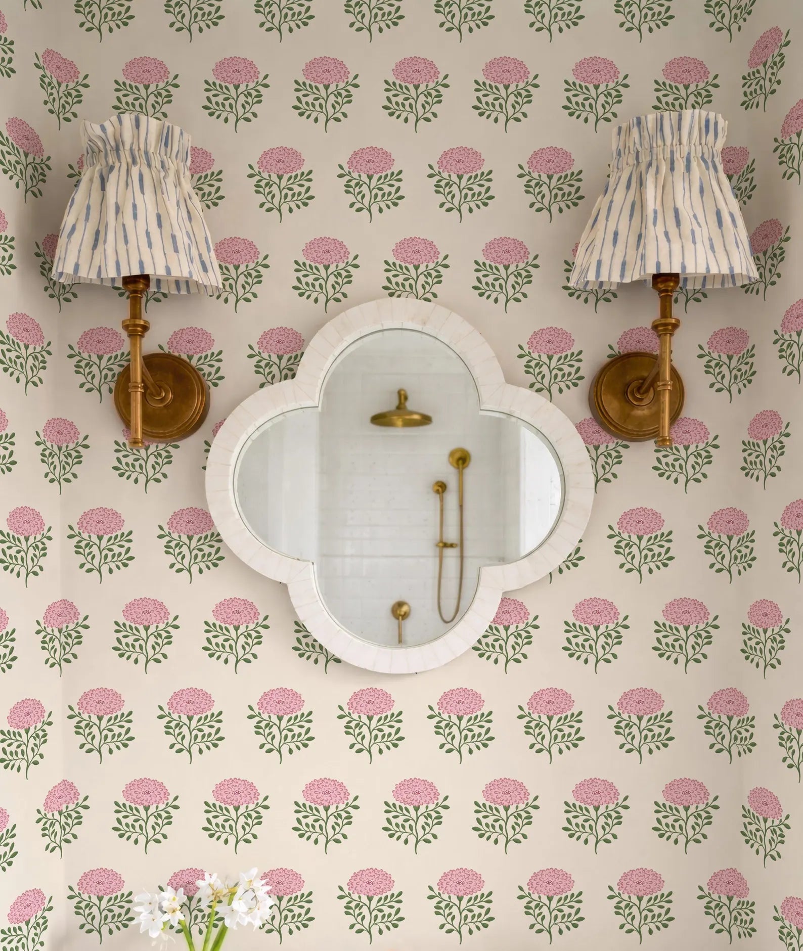 a bathroom with a floral wallpaper pattern, a white oval mirror, and two wall sconces with striped fabric shades.