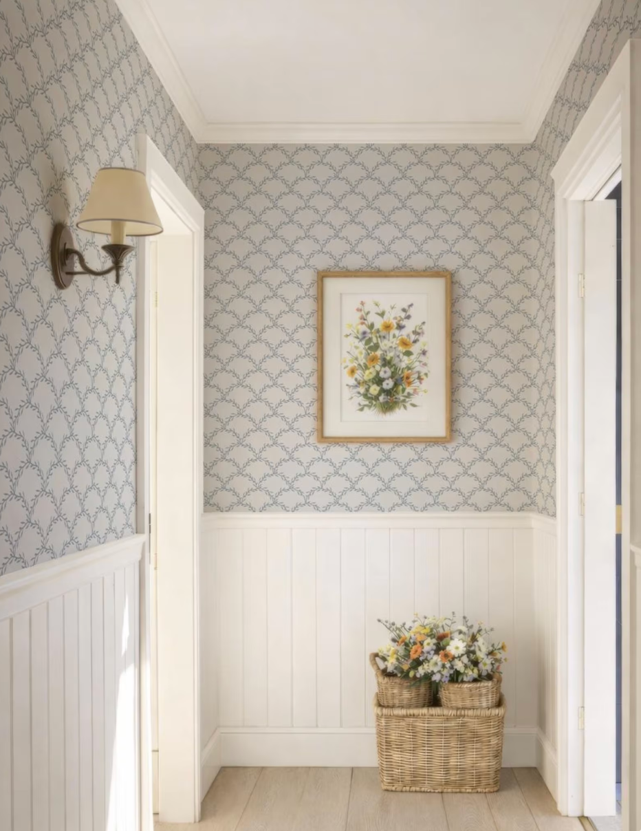 a hallway with a floral painting hanging on the wall, a wicker basket filled with flowers, and a wall lamp.
