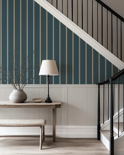 a wooden table with a lamp, a vase with branches, and a bench. The table is situated in front of a staircase with a black railing. The walls are painted in a blue and white color scheme, and the floor is made of wood.