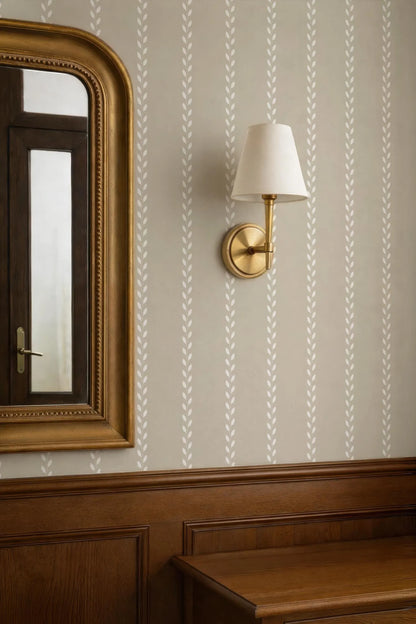 a wallpapered wall with a gold-framed mirror and a wall-mounted lamp with a white shade.