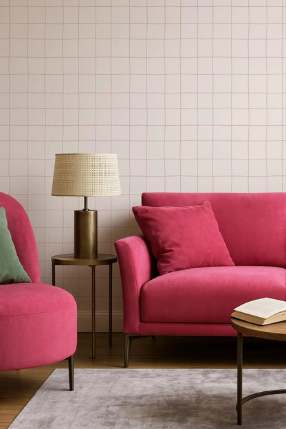 a cozy living room with a pink sofa, a red armchair, and a wooden coffee table. The room has a grid-like pattern on the walls, and there is a lamp on a side table next to the sofa.