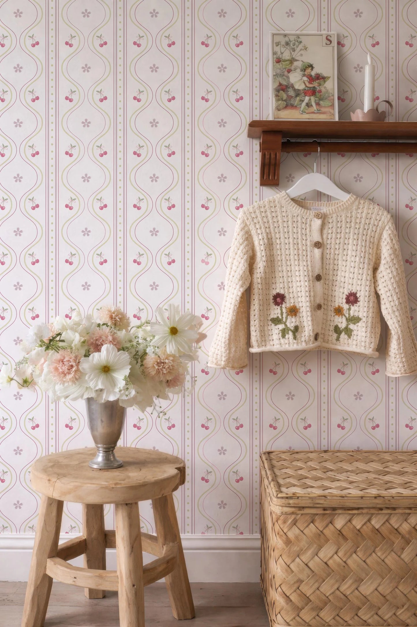 a cozy and charming interior with a wooden stool, a vase of flowers, a wooden shelf with a sweater, and a woven basket. The wall behind these items is adorned with a floral wallpaper pattern.