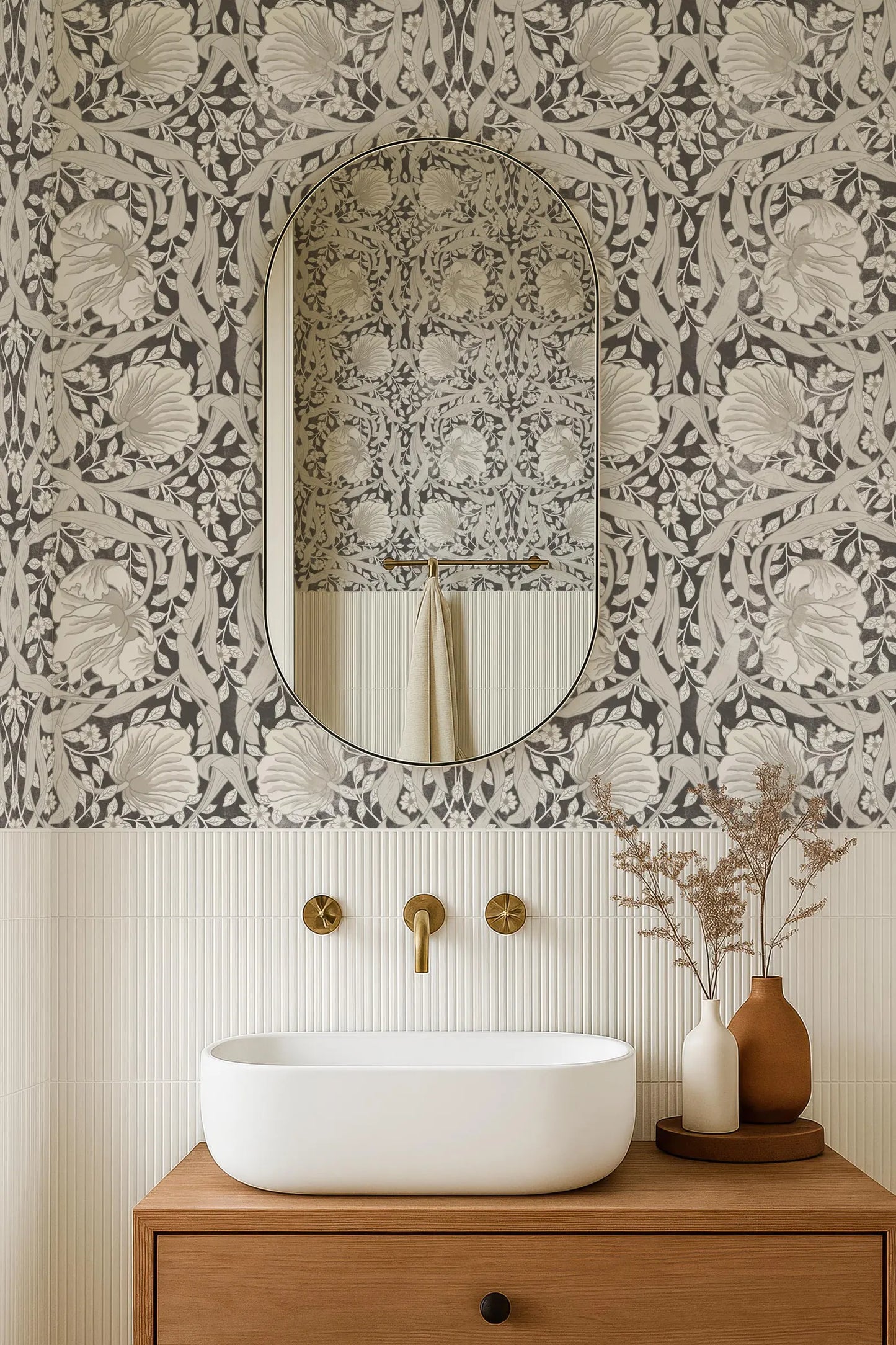a bathroom with a white sink, a mirror, and a vase with flowers on a wooden cabinet. The wall behind the sink has a floral wallpaper pattern.