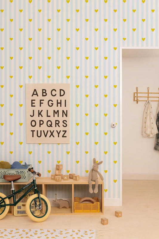 a child's bedroom with a blue and white striped wallpaper, a wooden toy shelf, and a bicycle. The wall is decorated with a large alphabet sign, and there are various toys and stuffed animals scattered throughout the room.