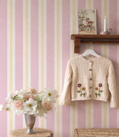a cozy and charming scene with a pink and white striped wall, a wooden shelf displaying a sweater with flowers, and a vase of white and pink flowers.