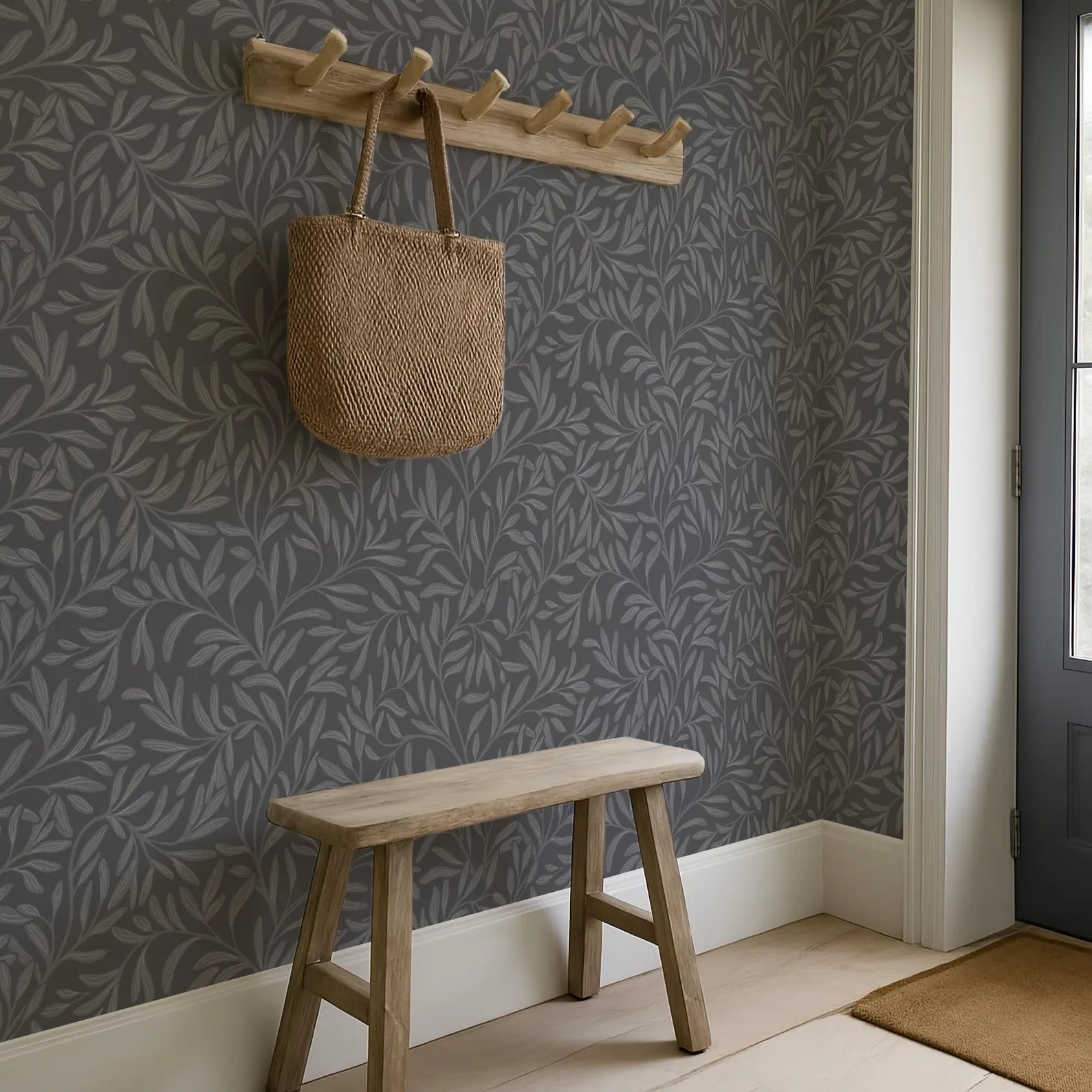 a wooden bench with a woven bag hanging on a wooden coat rack above it, set against a gray wall with a leaf-patterned wallpaper.