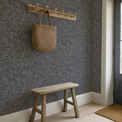 a wooden bench with a woven bag hanging on a wooden coat rack above it, set against a gray wall with a leaf-patterned wallpaper.