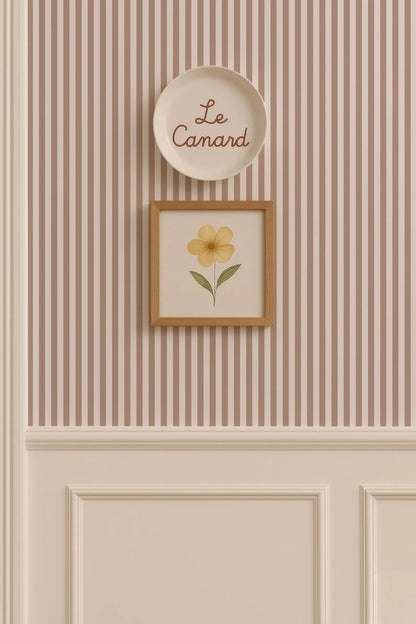 a wall with a framed picture of a yellow flower and a plate with the word "Le Camand" written on it.