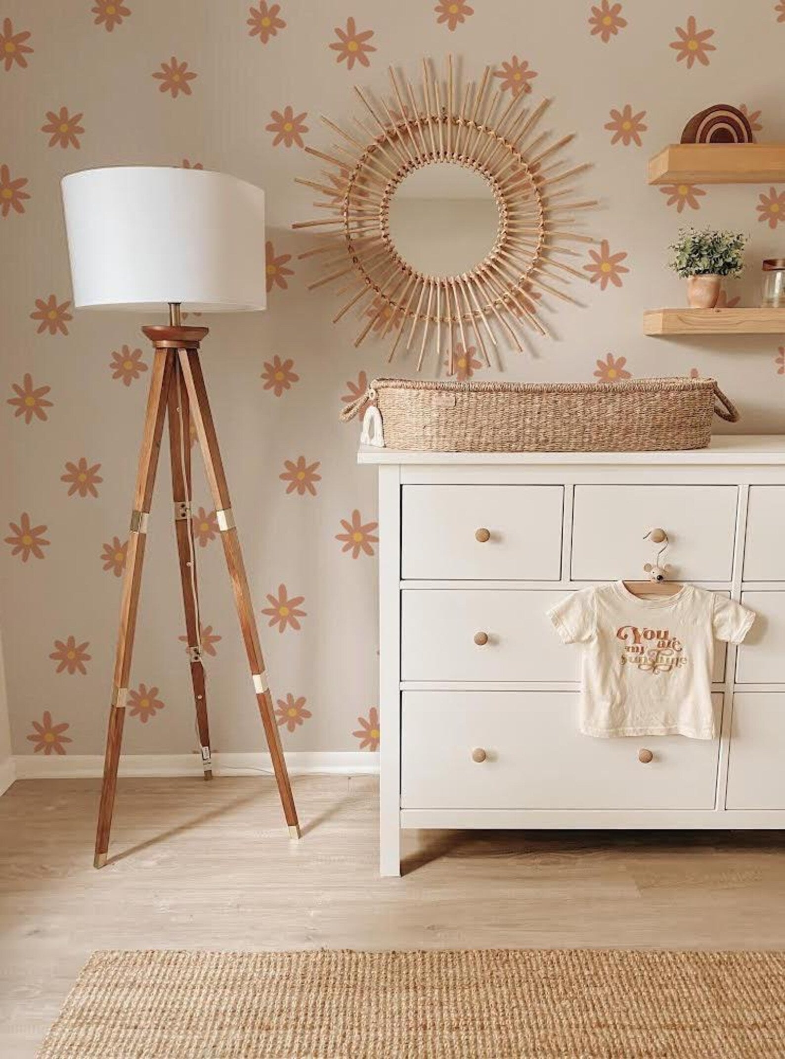a cozy and well-organized nursery room with a white dresser, a wooden tripod lamp, a woven basket, and a decorative sunburst mirror on the wall.