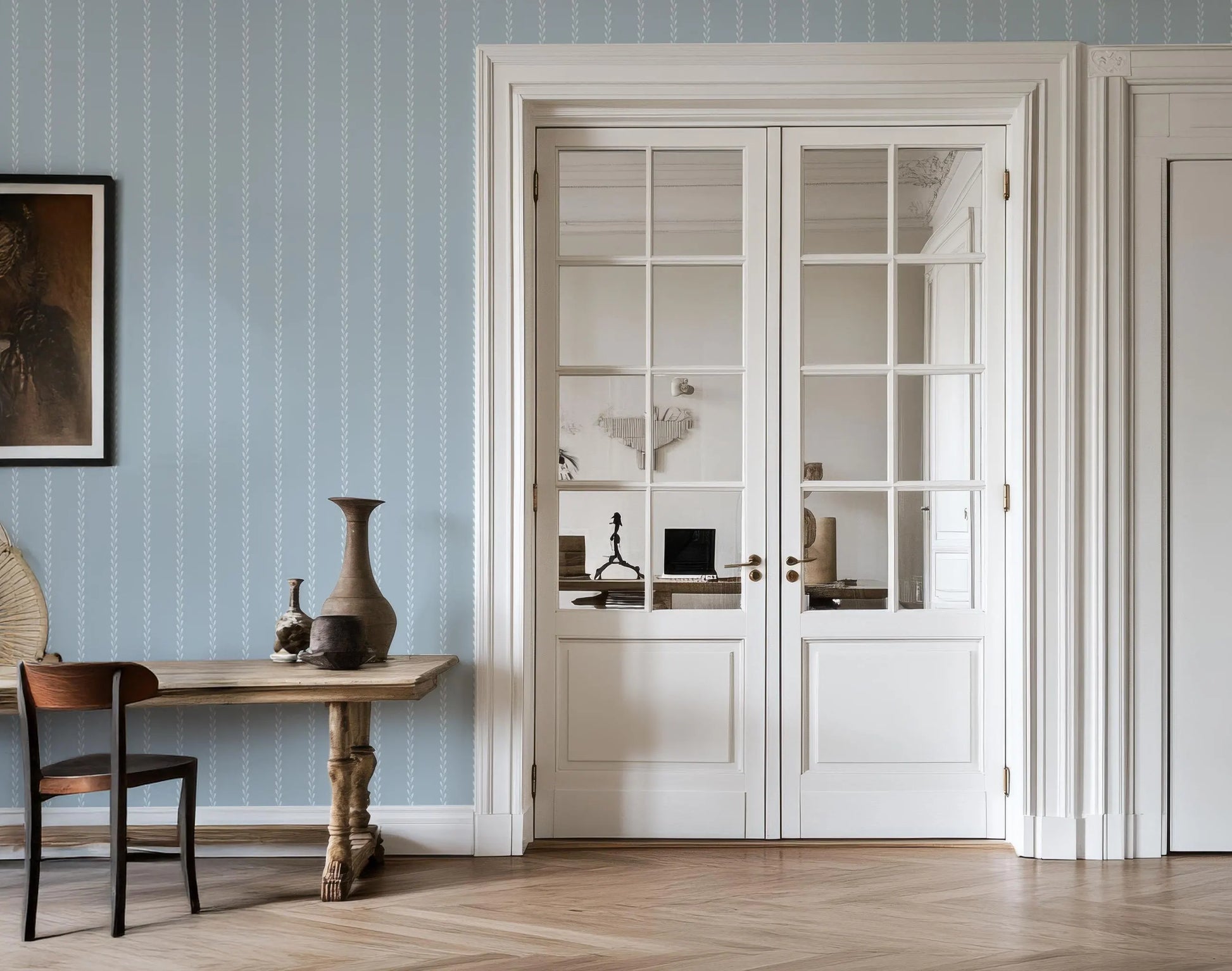 a room with a wooden table, a vase, and a chair. The room has a blue and white color scheme, with a large window and white doors.