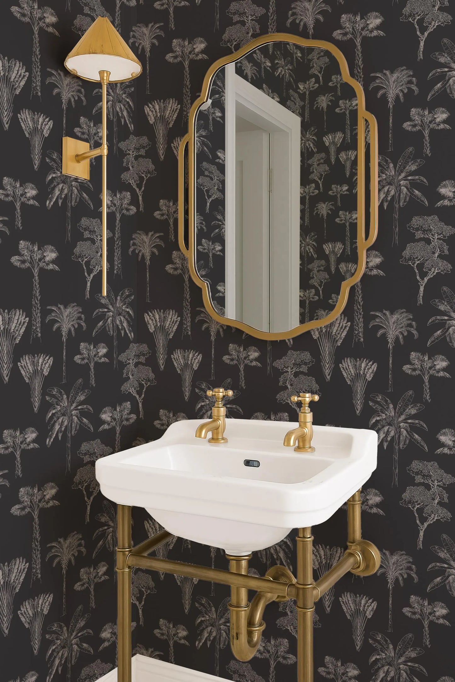 a bathroom with a white sink, a gold-framed mirror, and a black and white wallpaper with palm trees.
