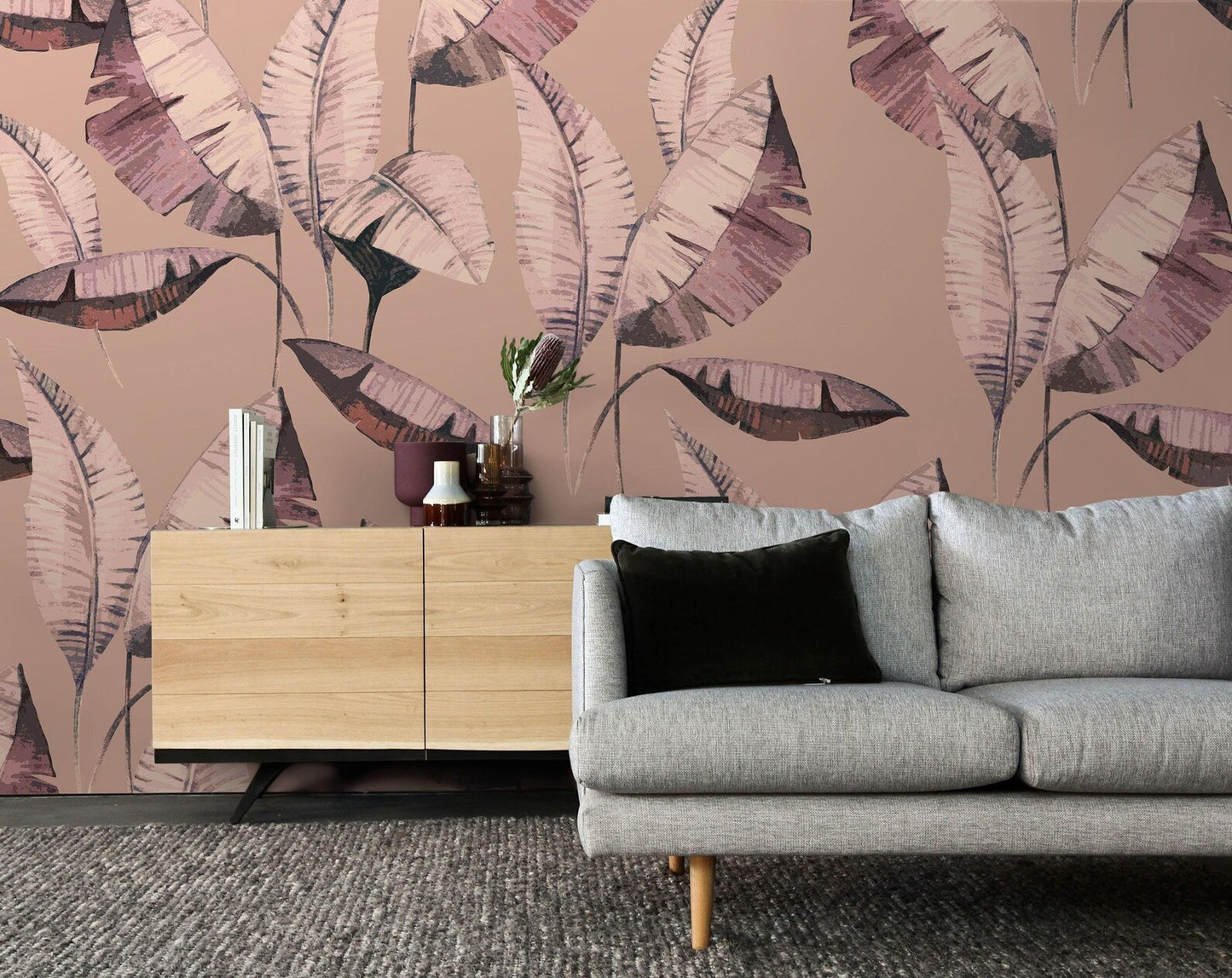 a living room with a gray sofa and a wooden cabinet against a wall with a large, colorful, leaf-like wallpaper.
