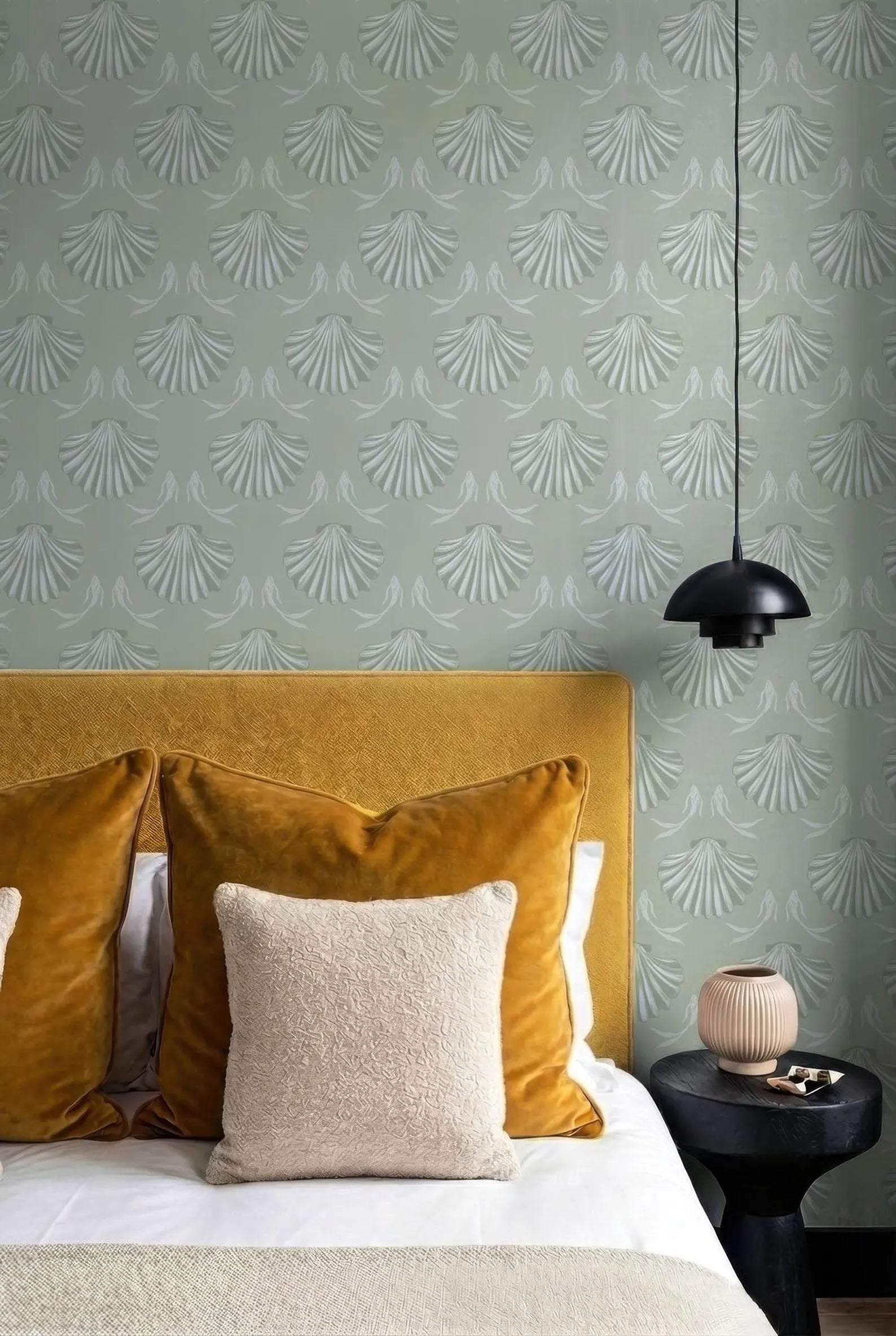 a bedroom with a yellow headboard, a black bedside table, and a hanging light fixture. The walls are covered in a patterned wallpaper, and the bed is adorned with yellow and beige pillows.