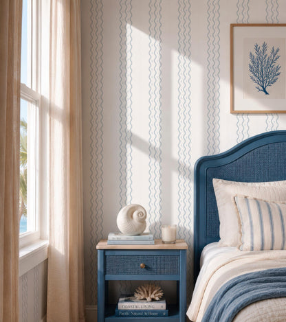 a serene and cozy bedroom with a blue headboard, a white bedspread, and a blue nightstand with a white lamp and a white vase. The room is decorated with a blue and white striped wallpaper, and there is a framed picture of a tree on the wall.