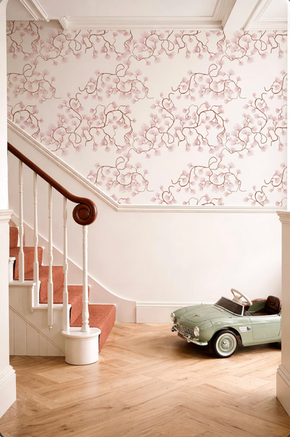 a vintage green toy car parked on a wooden floor next to a white staircase with a wooden handrail. The walls are decorated with a floral pattern, and the overall color scheme is predominantly pink and white.