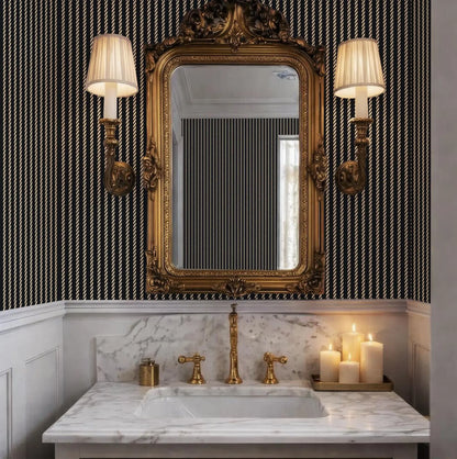 a luxurious bathroom with a marble vanity, a gold-framed mirror, and two wall sconces with white shades. The bathroom has a black and white striped wallpaper, and there are three lit candles on the vanity.