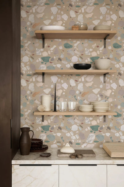 a kitchen counter with a variety of dishes and kitchenware displayed on it. The counter has three shelves, and the wall behind it has a patterned wallpaper. The items on the shelves include plates, bowls, and cups, as well as a vase. The overall scene suggests a well-organized and functional kitchen space.