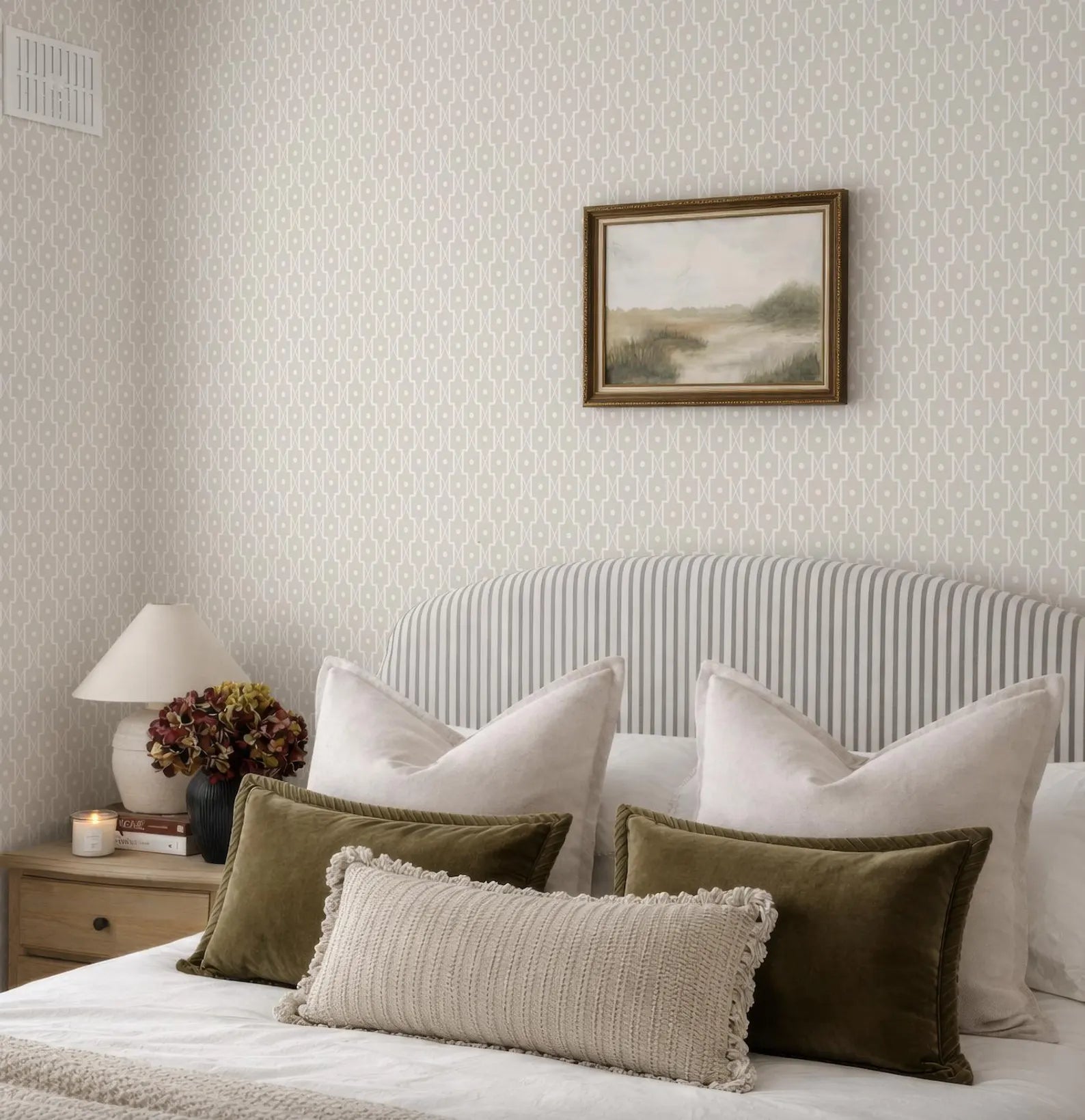 a well-decorated bedroom with a bed, a framed landscape painting on the wall, and a lamp on a nightstand.