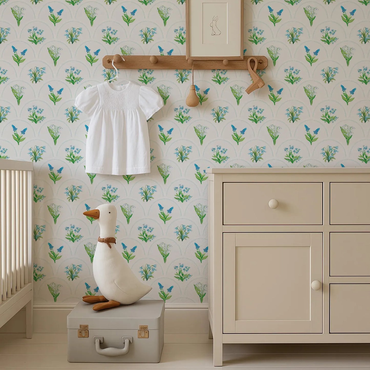 a nursery room with a white dresser, a stuffed duck, and a wallpapered wall with a floral pattern.